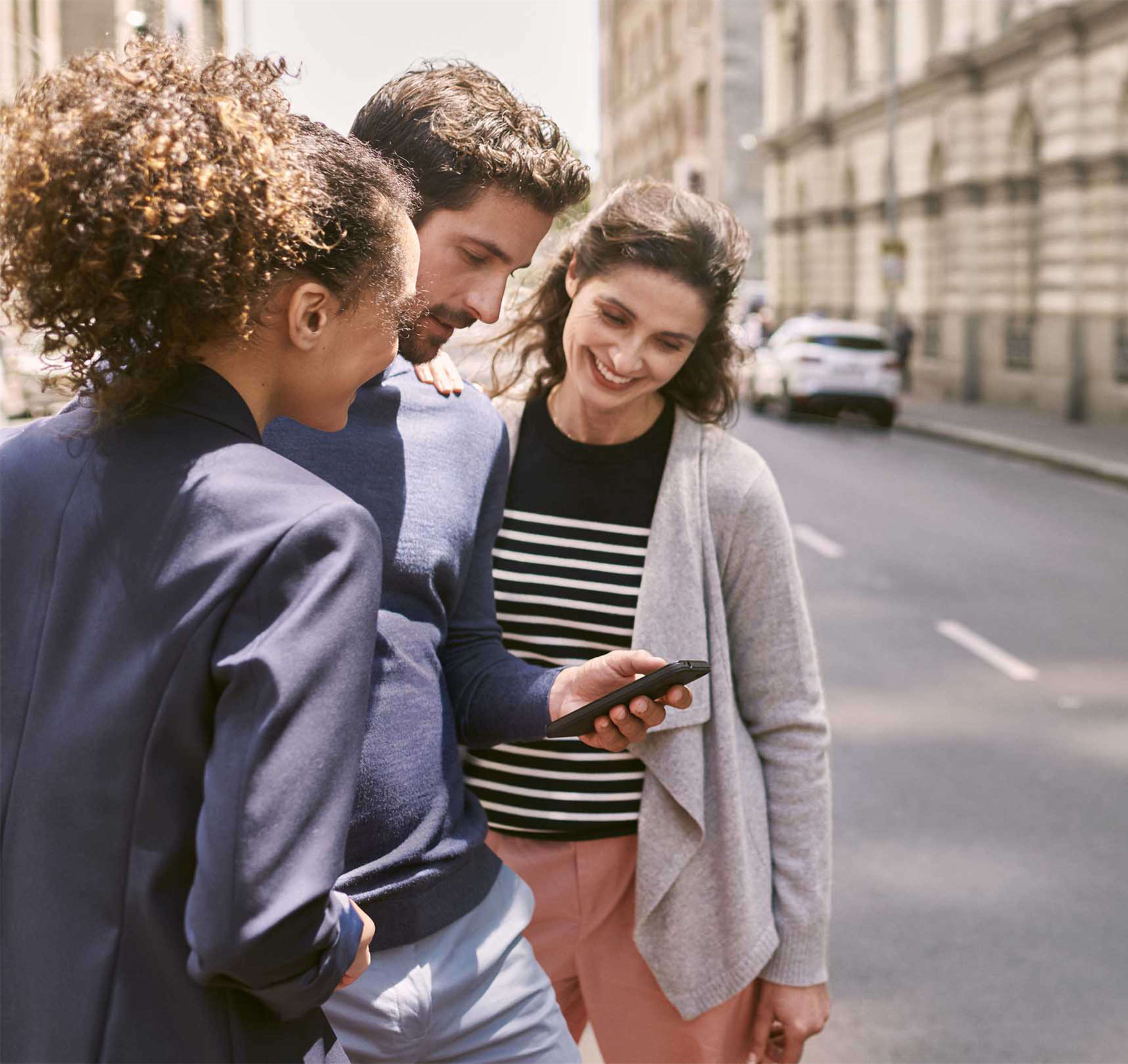 Чоловік і дві жінки дивляться на екран смартфона на вулиці